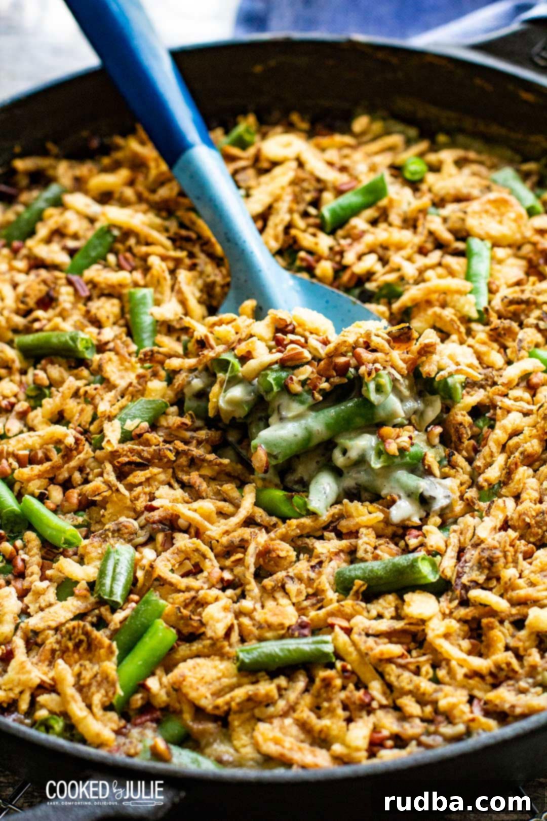 A serving spoon lifting a generous portion of creamy green bean casserole with golden fried onions from a baking dish
