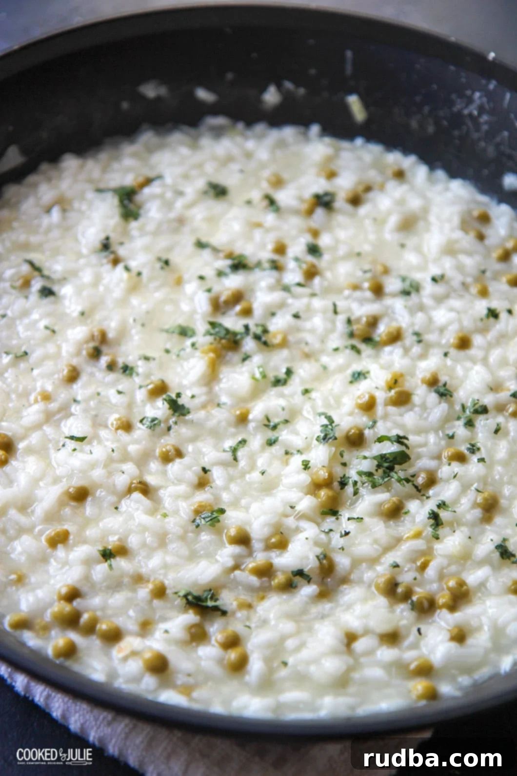 Creamy Parmesan and Pea Risotto in a black skillet, garnished with fresh herbs