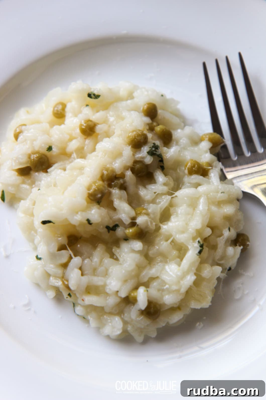 A serving of creamy Parmesan risotto with green peas on a white plate, with a fork