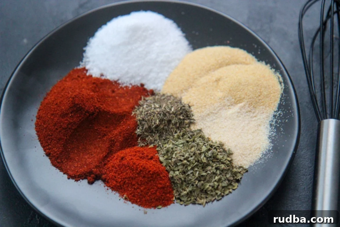 Seven different spices laid out on a black plate with a whisk, before mixing