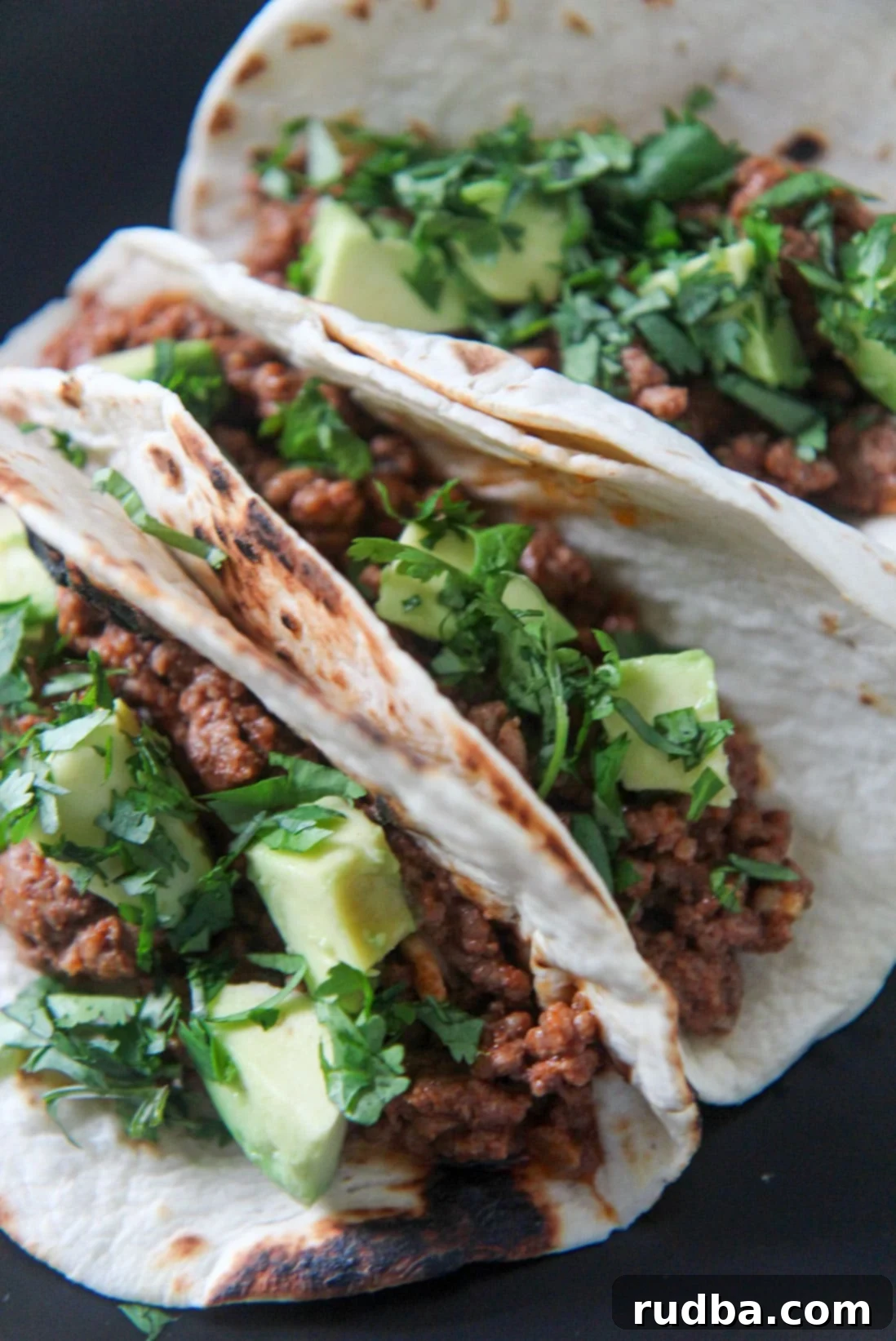 three Cajun beef tacos on a black plate 