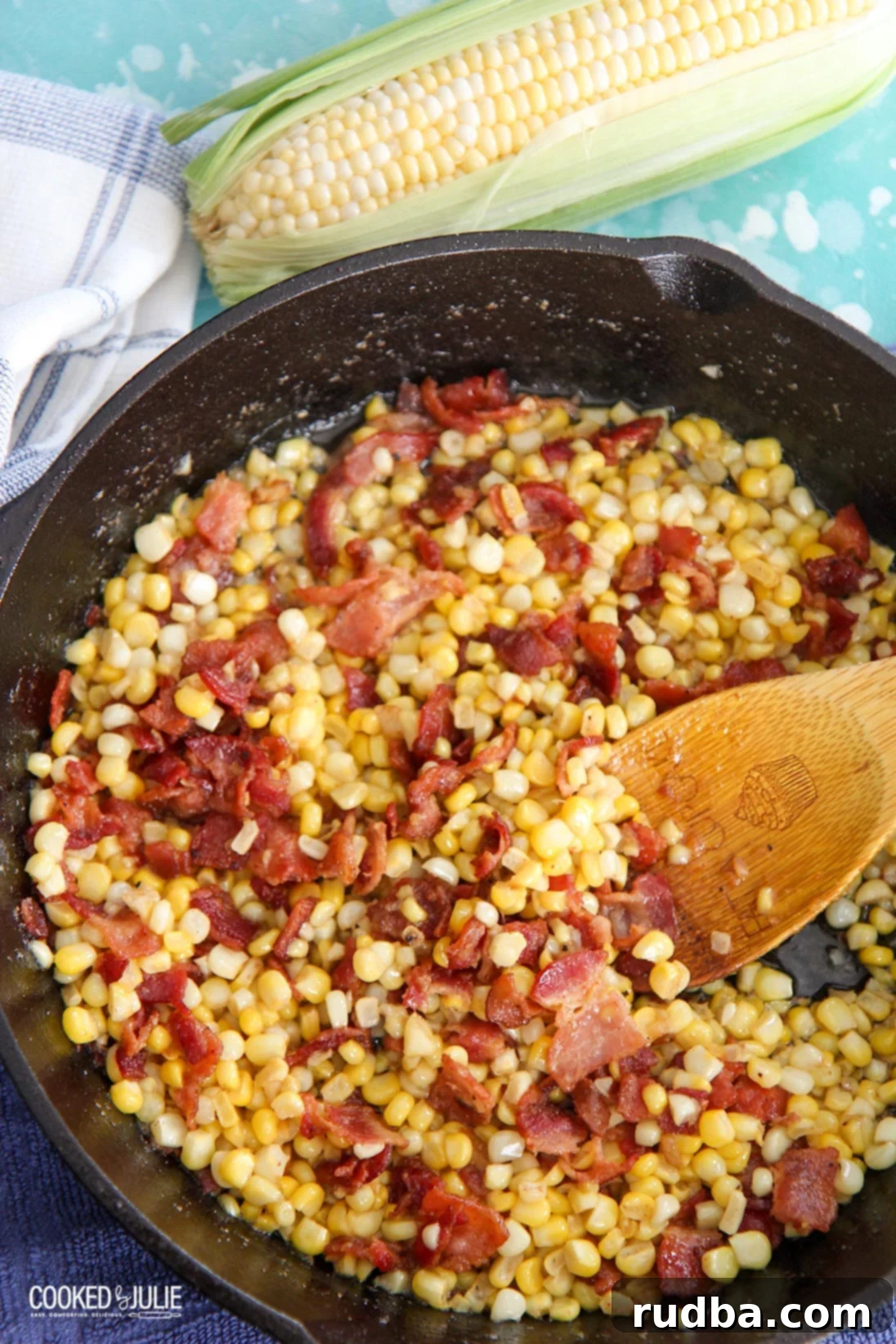 corn and bacon in a cast iron skillet with a wooden spoon 