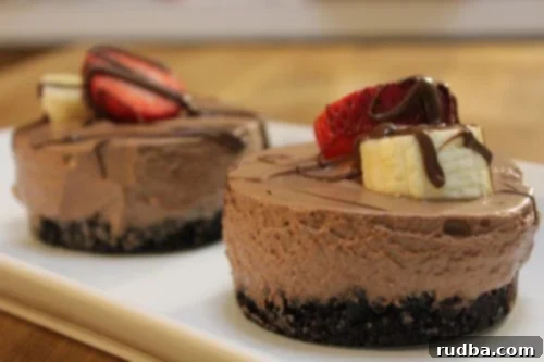 Two Nutella mousse servings with strawberries, bananas, and melted Nutella on top. Served on a white plate.