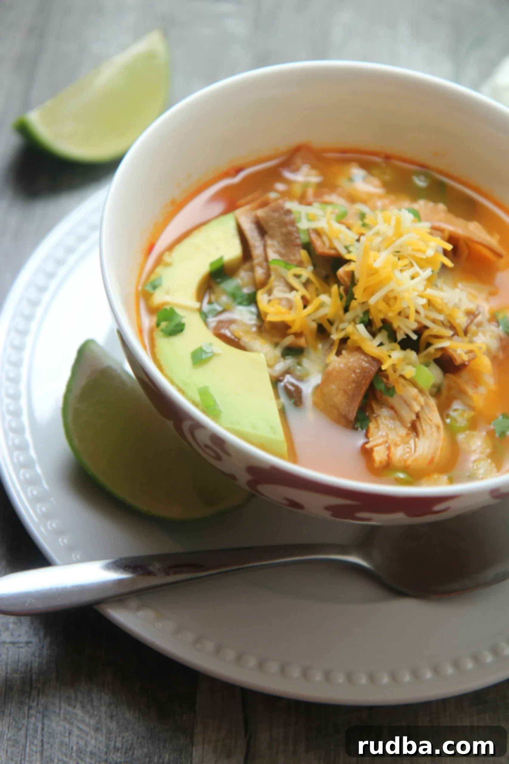 Spicy chicken tortilla soup in a white and red bowl with a spoon