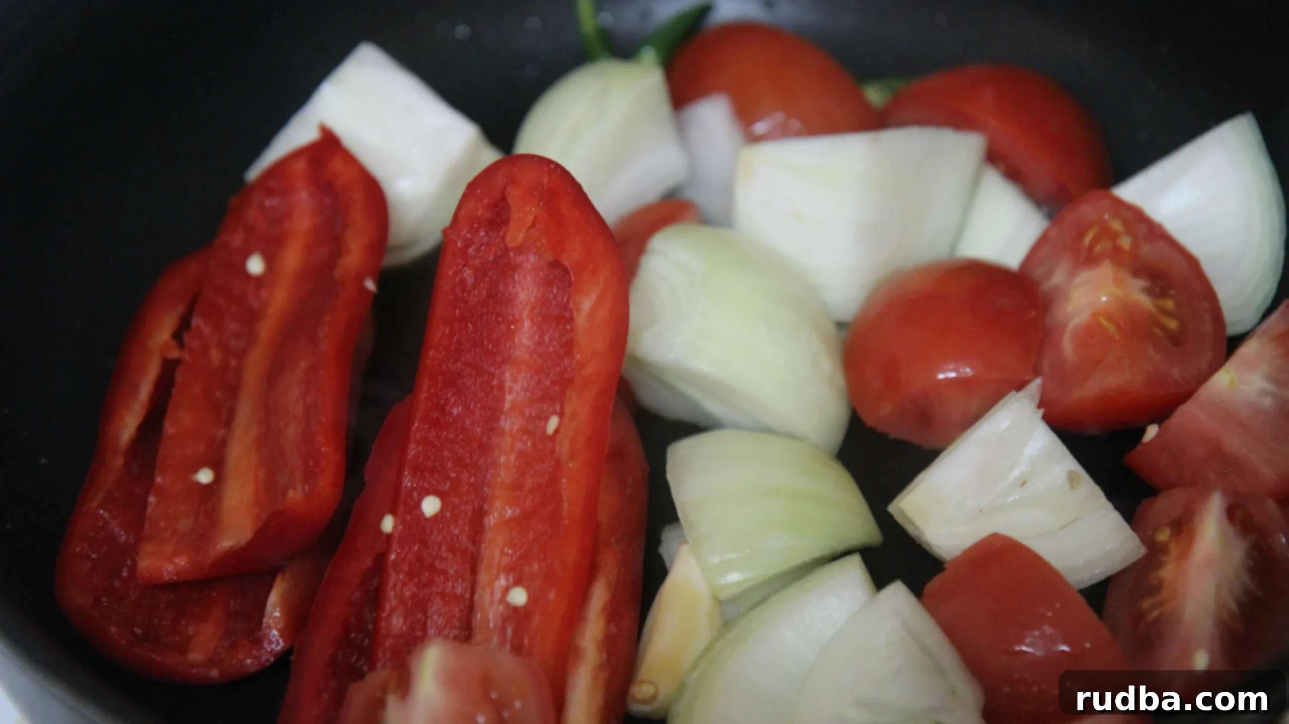 raw peppers, onions, and tomatoes in a black skillet.