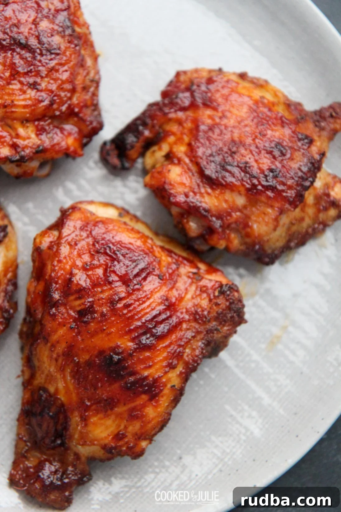 Fall-Off-The-Bone Oven BBQ Chicken 2 Three perfectly baked BBQ chicken thighs resting on a gray plate, glistening with sauce and ready to be served.