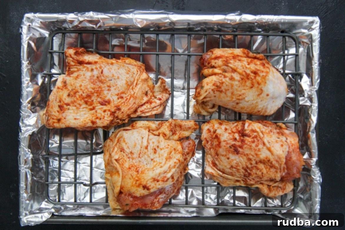 Fall-Off-The-Bone Oven BBQ Chicken 3 Four pieces of raw, seasoned chicken thighs laid out on a baking sheet, ready for the oven.