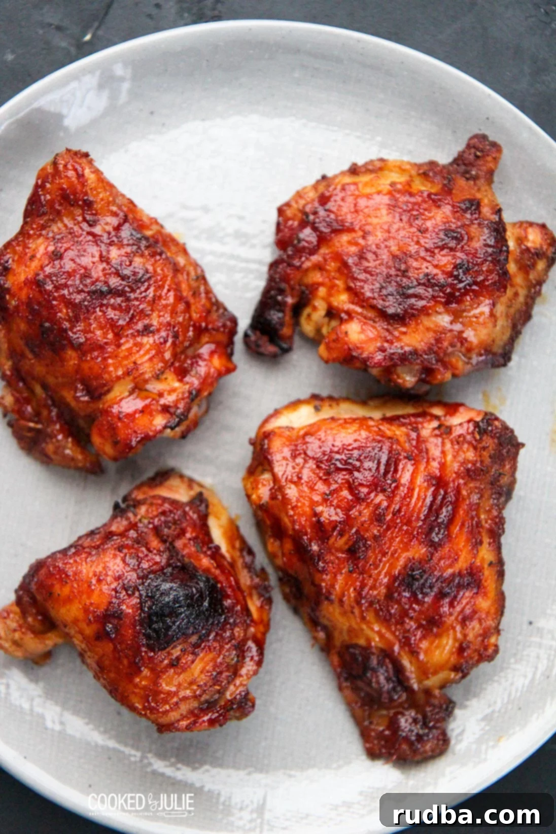 Fall-Off-The-Bone Oven BBQ Chicken 4 Four glistening, cooked BBQ chicken thighs arranged on a platter, ready to be served.