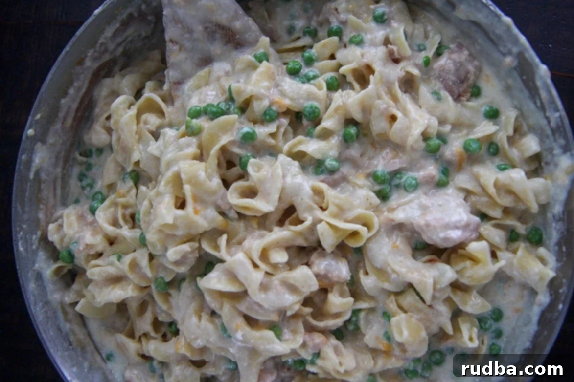 Creamy sauce with egg noodles, peas, and tuna in a large skillet, mixed and ready for baking