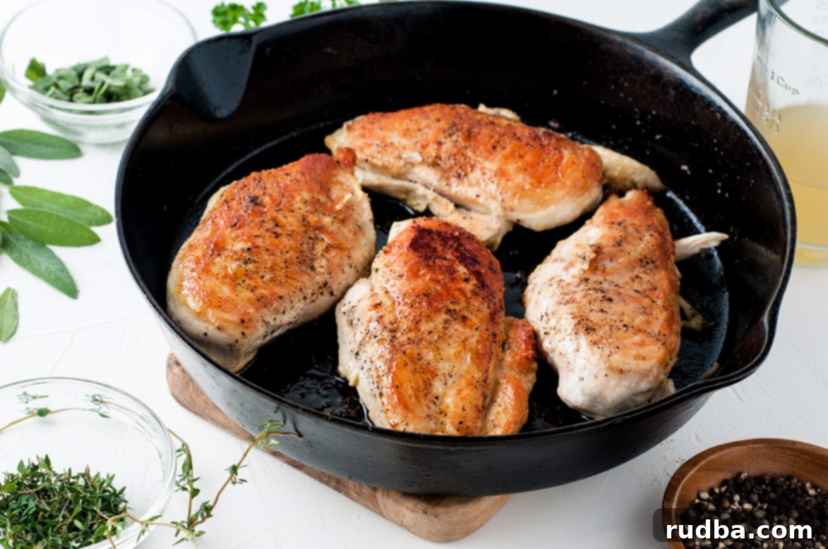 Four perfectly cooked chicken breasts sizzling and golden brown in a well-seasoned cast iron skillet.