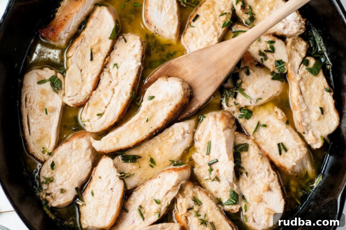 Close-up of perfectly sliced garlic cajun chicken pieces in a black skillet, glistening with savory herb butter sauce, next to a wooden spoon.
