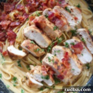 A top-down view of creamy chicken and bacon pasta in a skillet, garnished with fresh herbs, indicating a complete dish ready to be served.