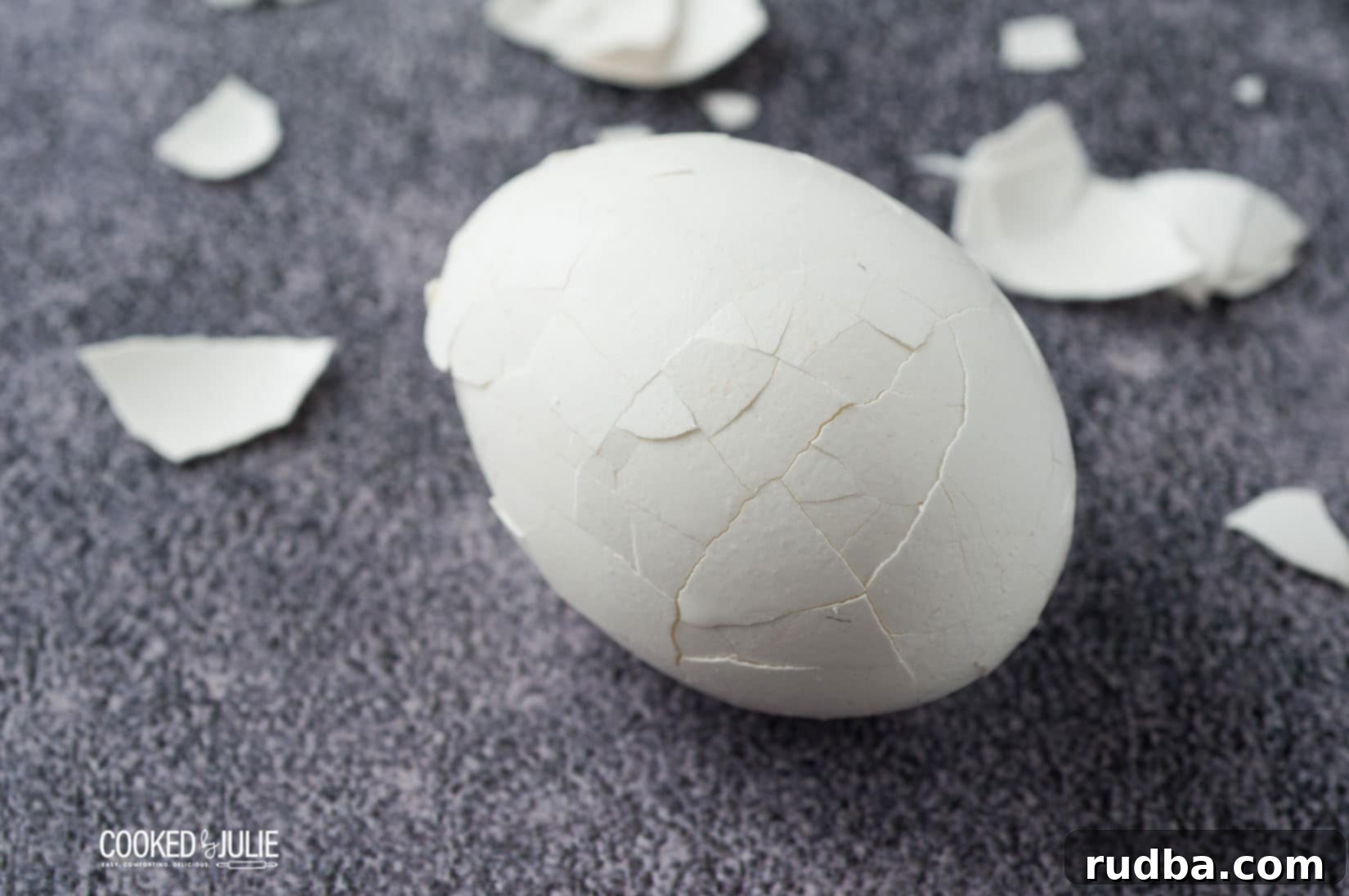 A white hard-boiled egg with its shell cracked in several places, surrounded by discarded shell pieces on a blue background