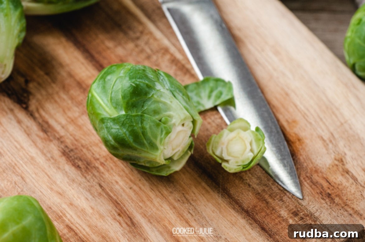 A sharp knife slicing Brussels sprouts in half on a rustic wooden cutting board