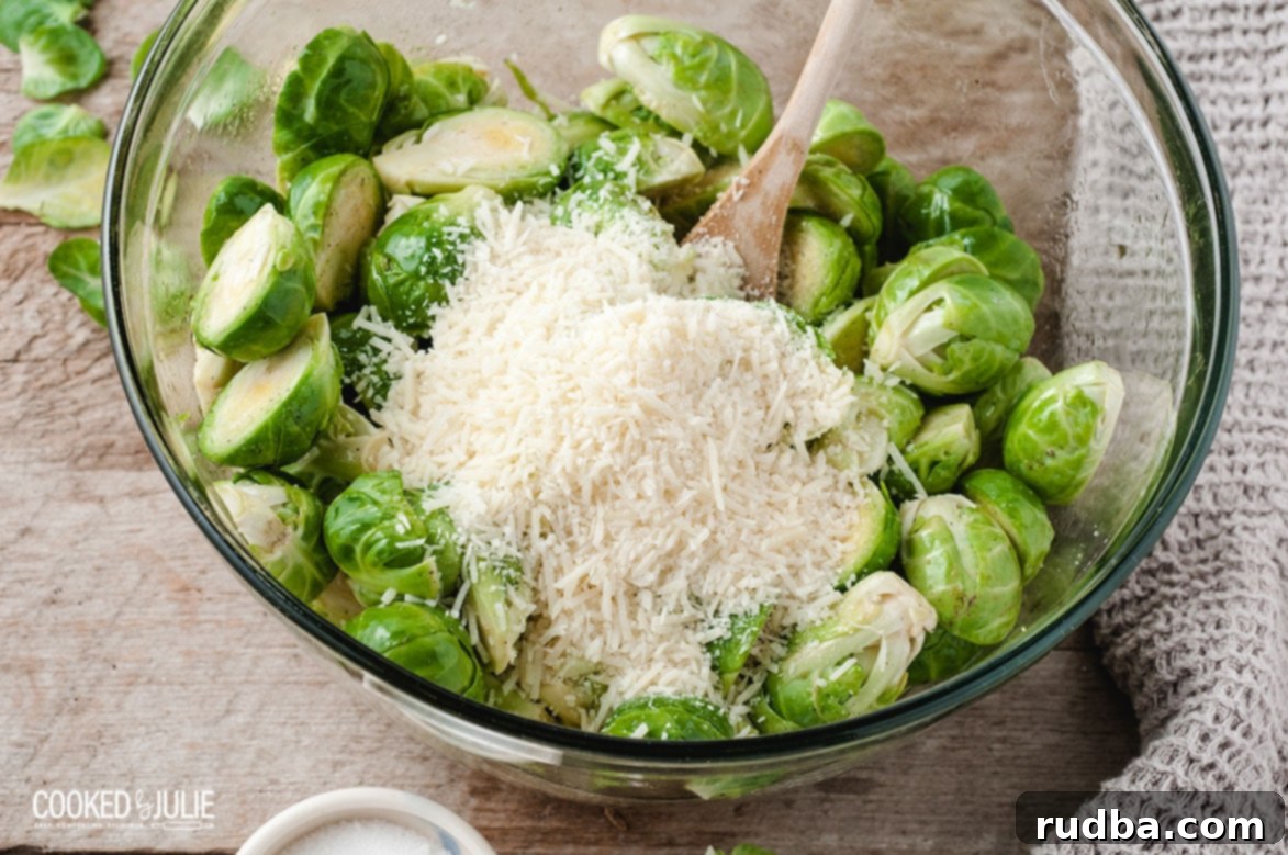 Parmesan cheese being mixed with olive oil coated Brussels sprouts in a large white bowl using a wooden spoon