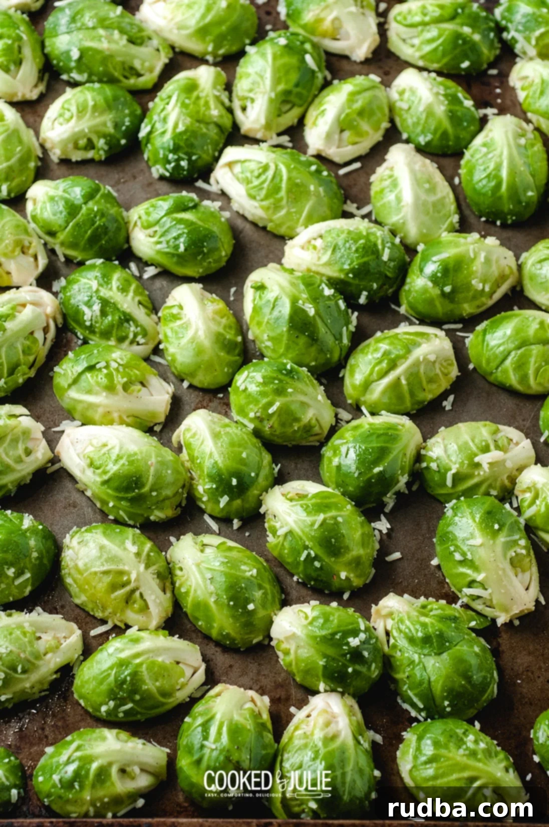 Parmesan-coated Brussels sprouts halves spread in a single layer on a parchment-lined baking sheet, ready for roasting