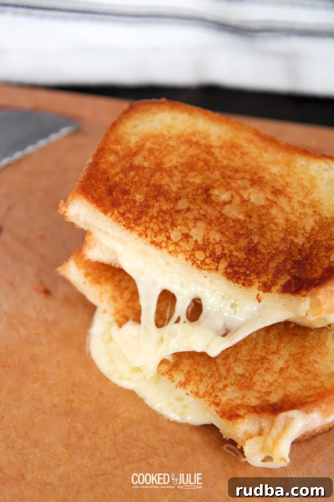 a perfectly grilled cheese sandwich cut in half, revealing gooey cheese, next to a knife