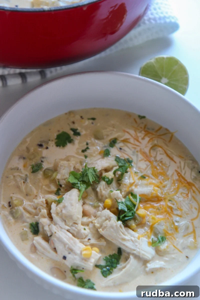 A bowl of creamy white chicken chili garnished with fresh cilantro and a lime wedge on the side, ready to be served.