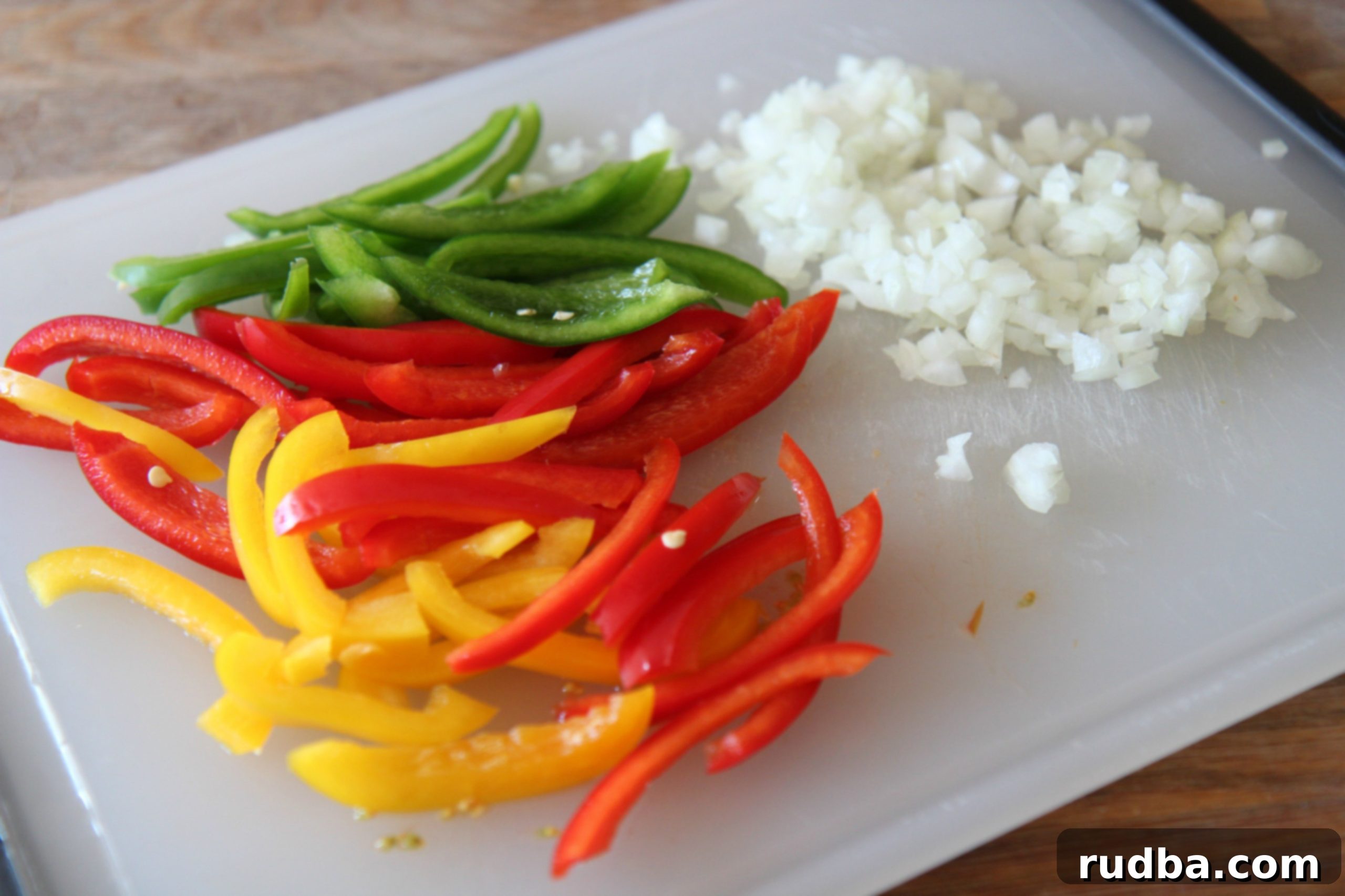 Slice red, yellow, and green bell peppers and finely dice a small white onion for the fajita pasta sauce.