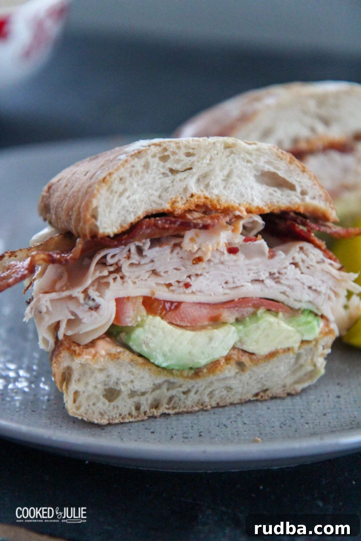 A perfectly assembled turkey bacon avocado sandwich, cut in half, revealing layers of fresh ingredients, served on a gray plate.