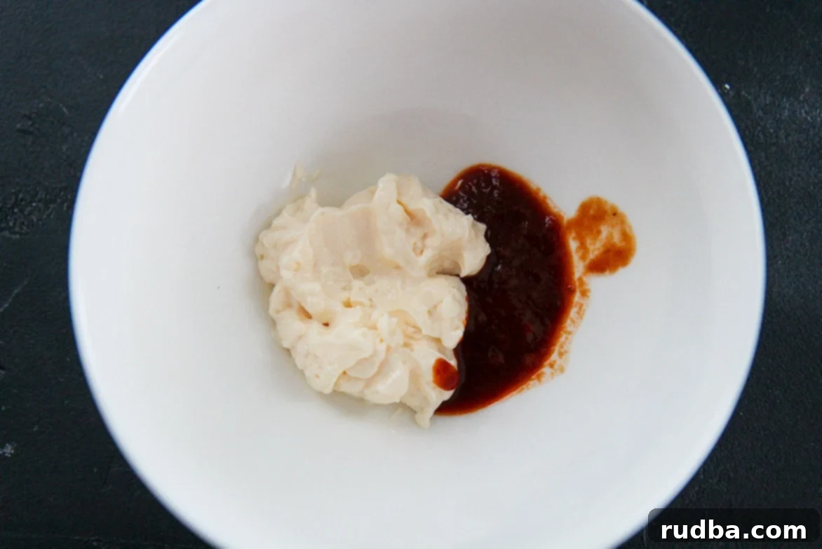 A pristine white bowl filled with creamy homemade chipotle mayo and a spoonful of chipotle sauce on the side, ready to be mixed.