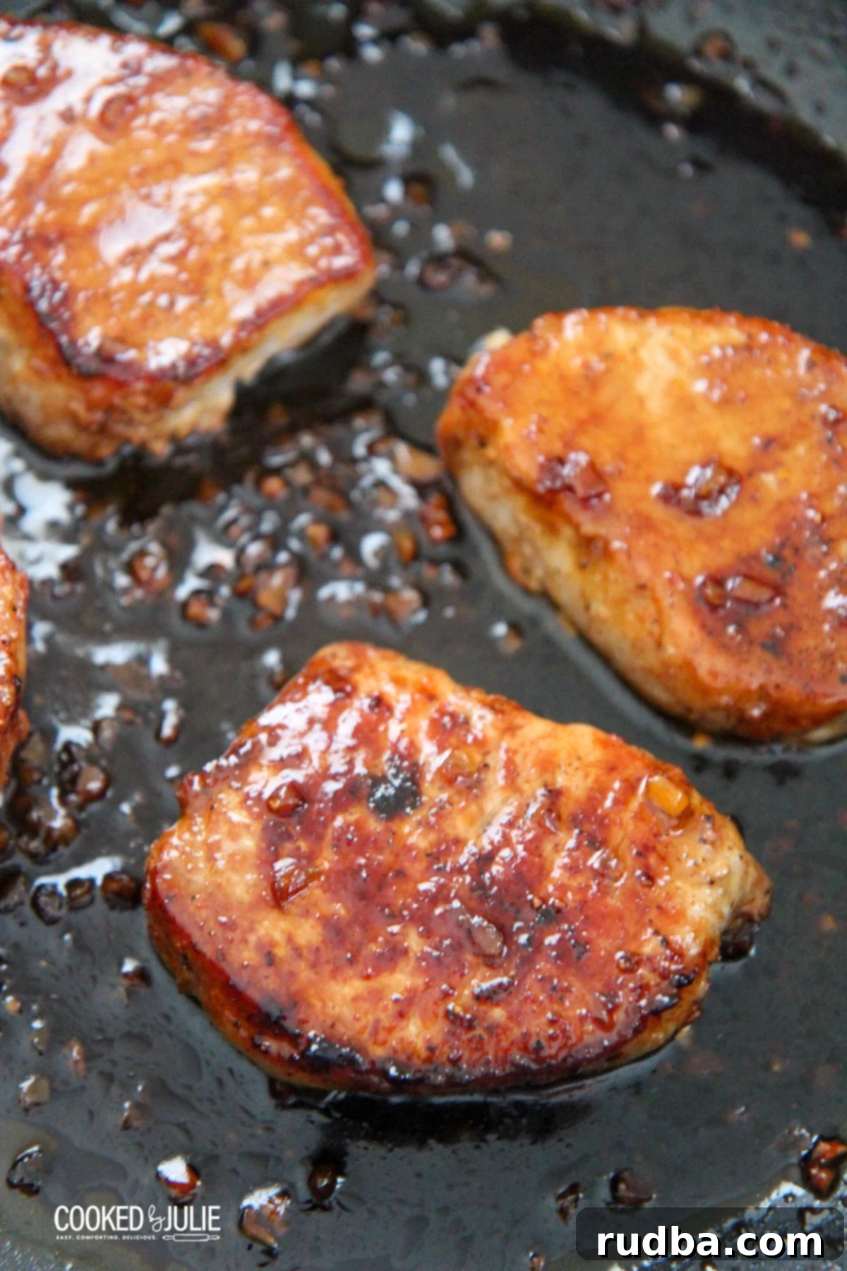 three honey garlic pork chops in a black skillet with fresh parsley garnish