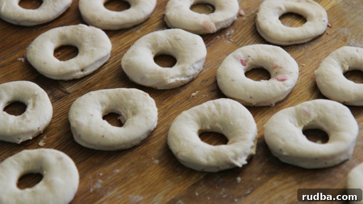 Neatly arranged donut cut outs on a wooden surface, ready for their second rise.