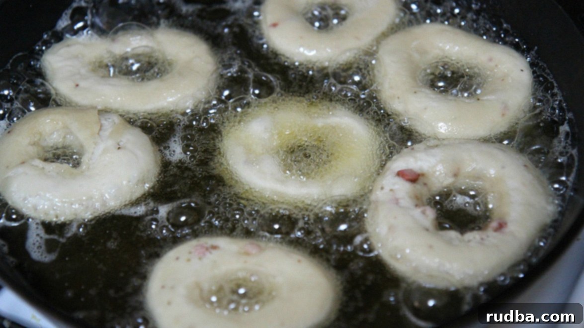 Delicious donuts frying in a skillet with shimmering hot oil, turning golden brown.