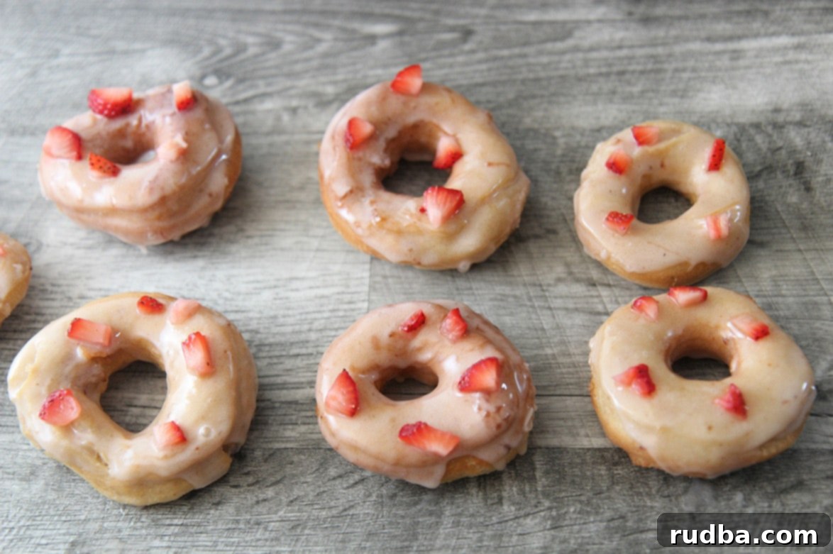 Six perfectly glazed strawberry donuts on a gray surface, ready to be enjoyed.