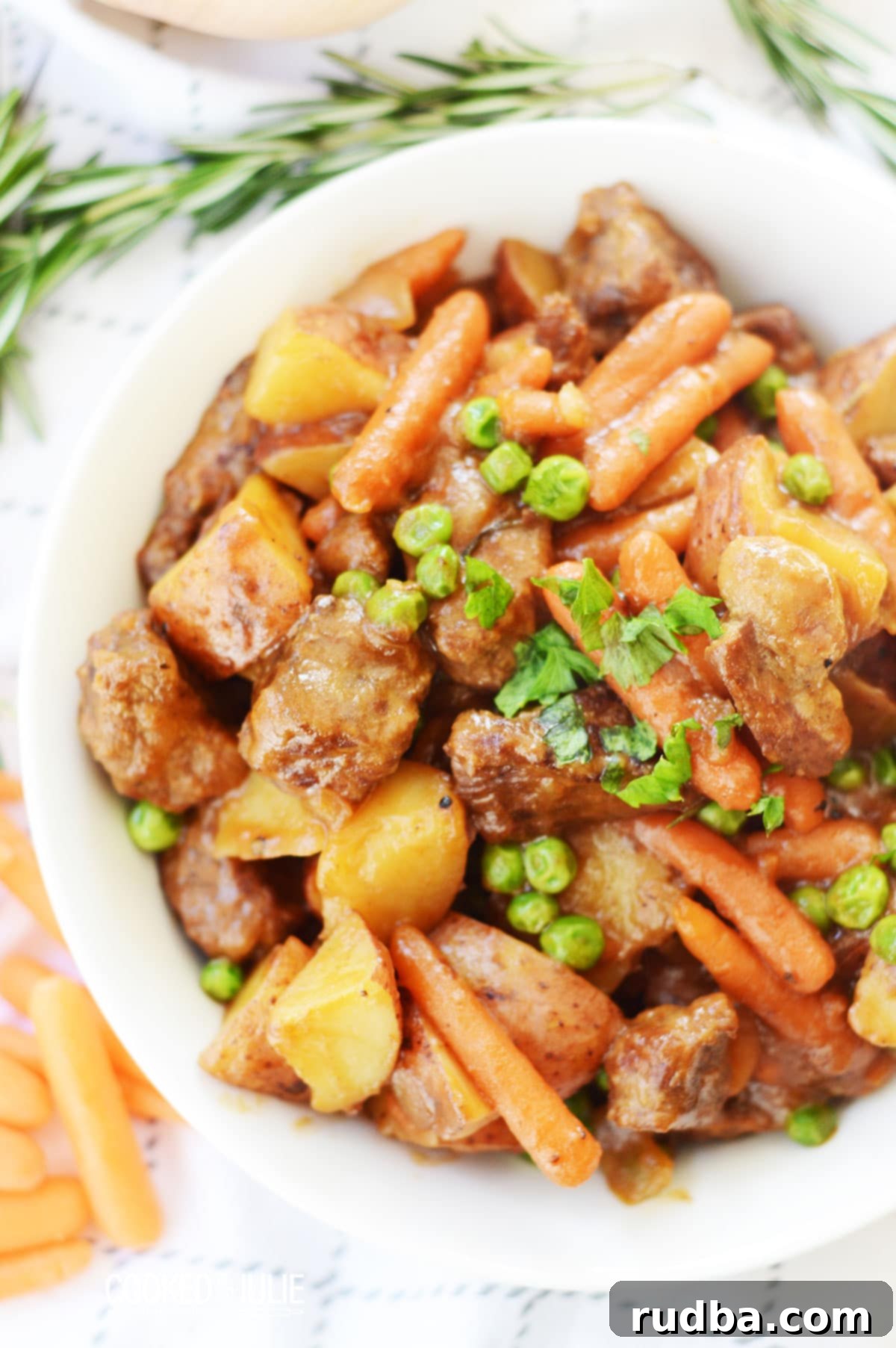 A steaming bowl of hearty beef stew garnished with fresh parsley and a sprig of rosemary.