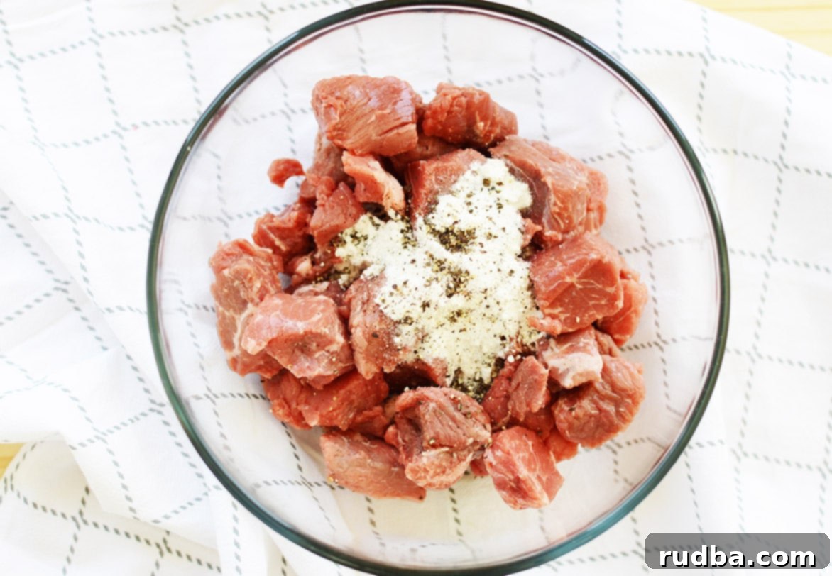 Raw beef chuck cubes coated in flour and spices, ready for searing, in a clear bowl.