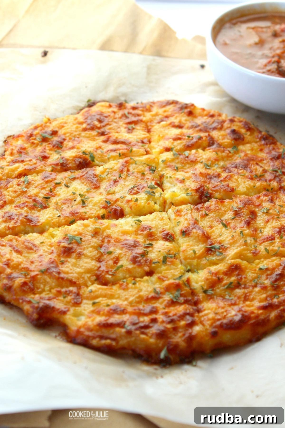 Delicious keto cheese bread on parchment paper, ready to be served, with a small bowl of sauce nearby.