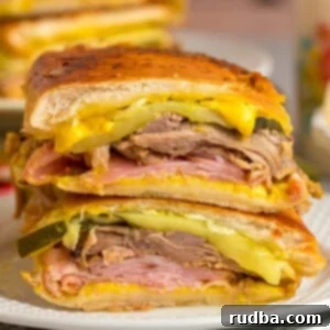 Classic Cuban Pressed Sandwich 2 Cuban sandwich sliced in half on a white plate.