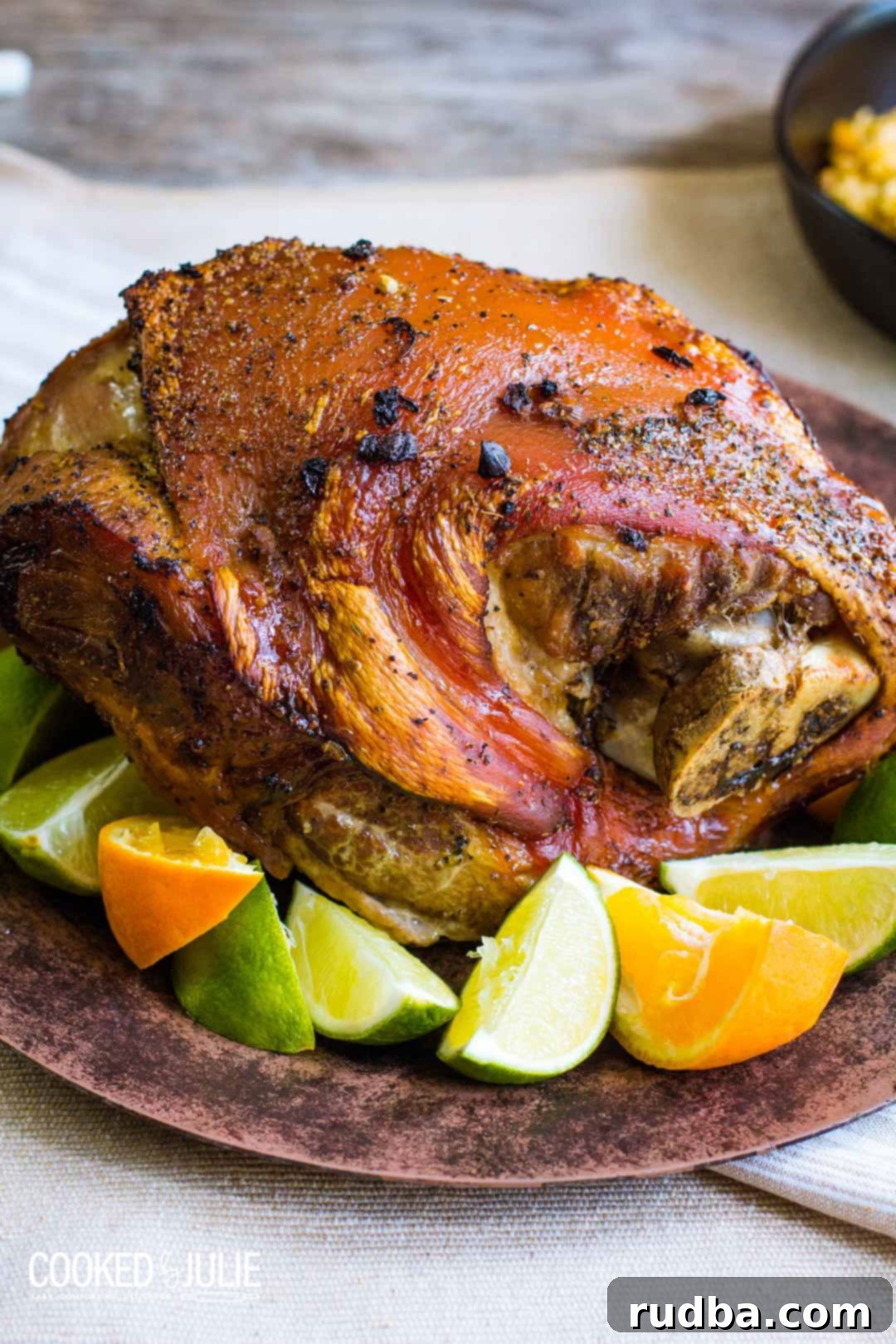 The Ultimate Cuban Pernil 2 Cuban Pernil on a brown plate with limes and oranges