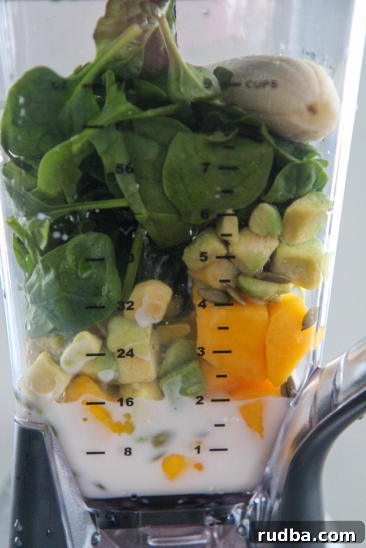 Spinach, mango, banana, avocado, and almond milk being blended together in a high-speed blender.