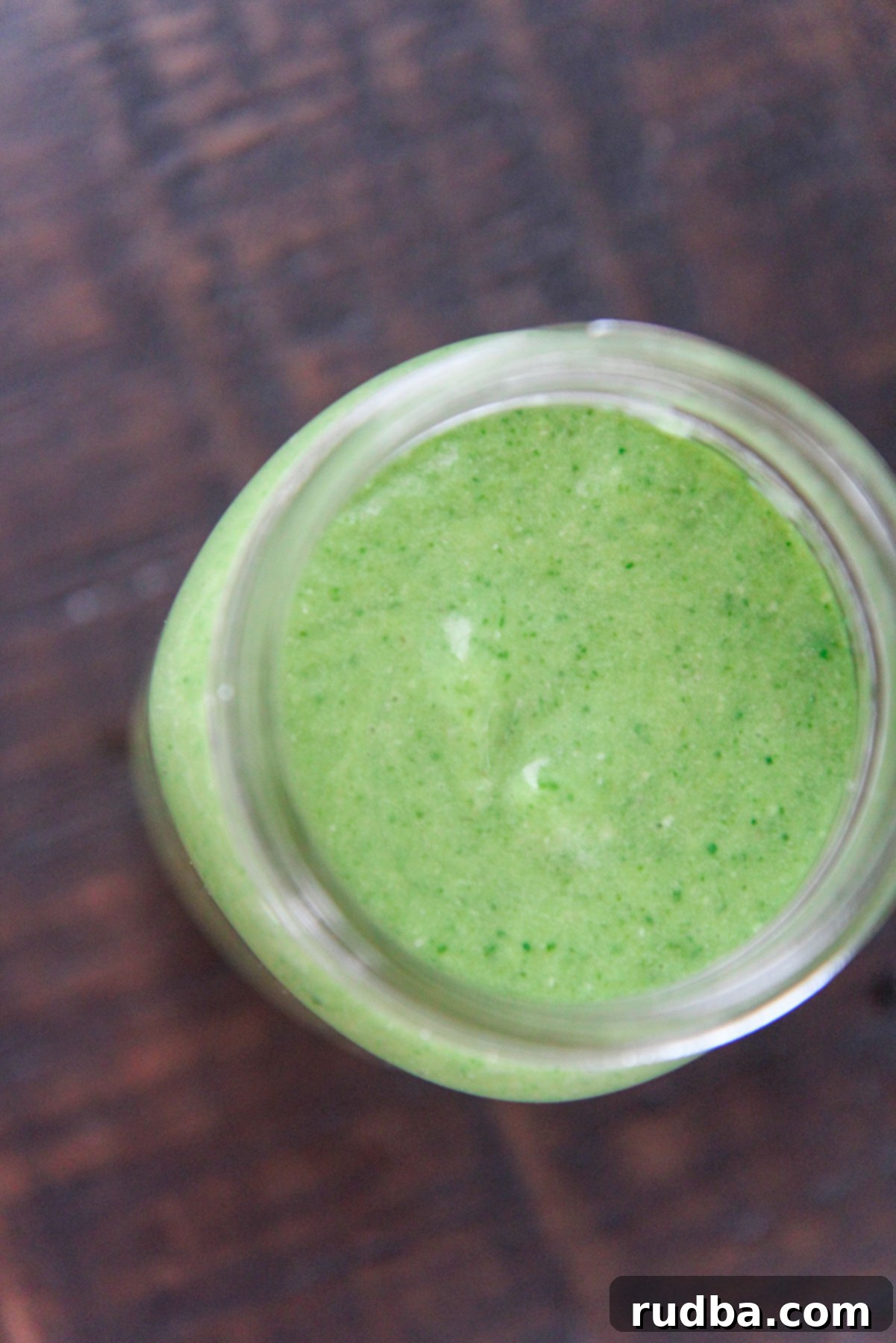 A filled mason jar of spinach avocado green smoothie placed on a rustic brown wooden table.