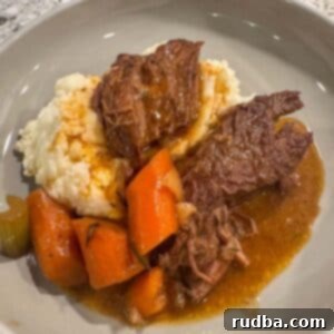 A delicious serving of slow cooker pot roast with gravy and vegetables next to a mound of creamy goat cheese mashed potatoes, garnished with fresh herbs.