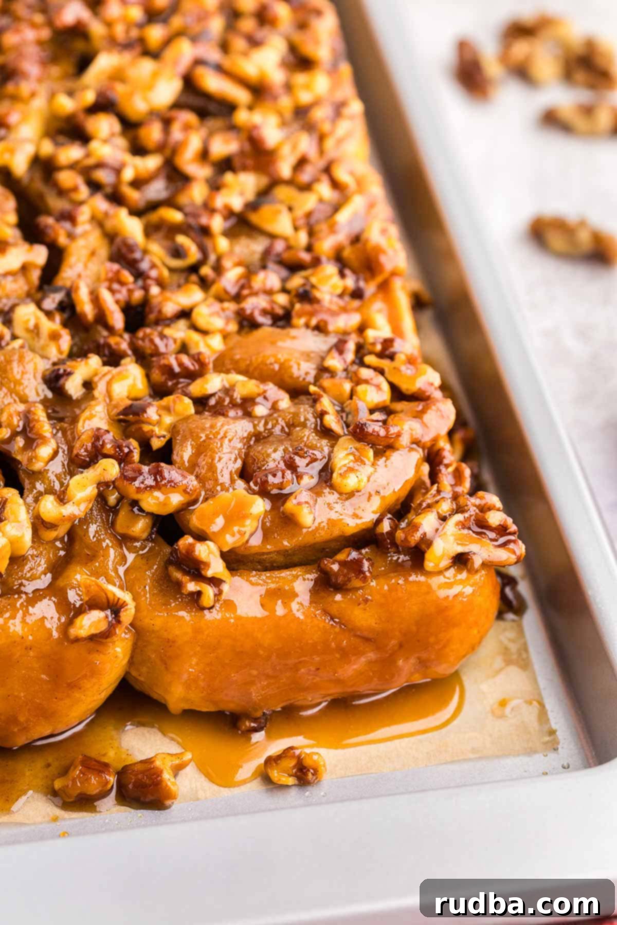 A close-up shot of twelve freshly baked sticky buns arranged on a platter, showcasing their rich, glossy caramel and chopped pecans.
