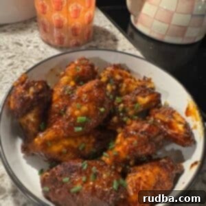 Cooked and sauced wings in a white bowl with a candle and tea kettle in the background.
